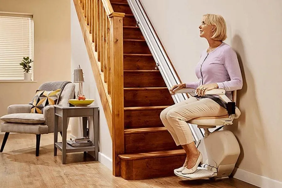 Straight stairlift in Colchester: woman seated on a stairlift beside a wooden banister